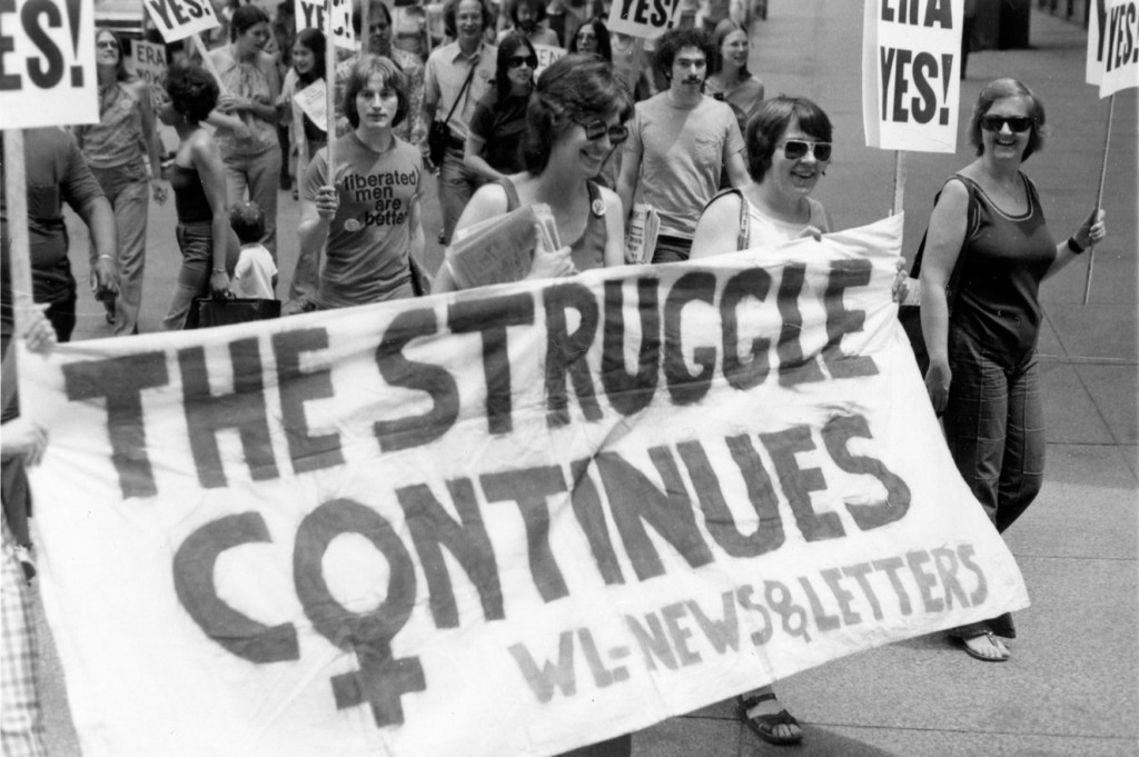 Suzanne French, Jane McKeever, and Mary Joan Schmidt holding banners and signs in an ERA march on 05/14/1977